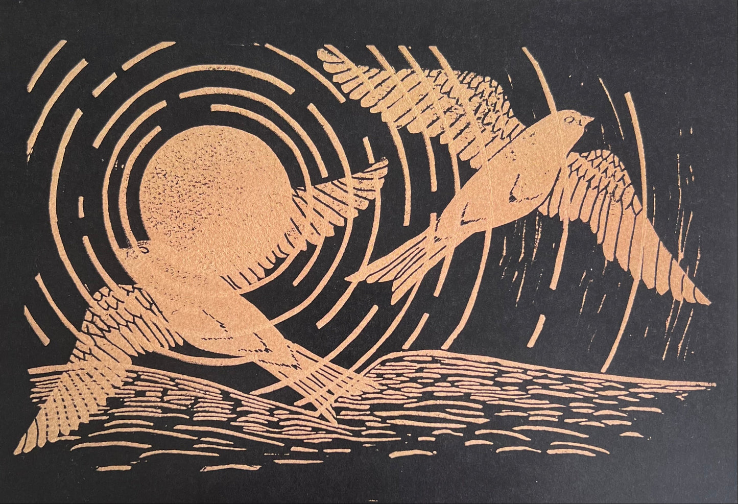 A greetings card depicting 2 gold swifts and a gold sun with concentric circles with gold landscape along the bottom edge.