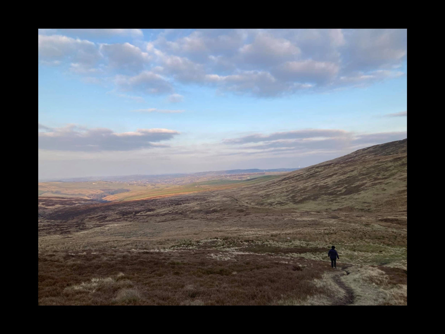 Person standing on a hill with a vast landscape and cloudy sky